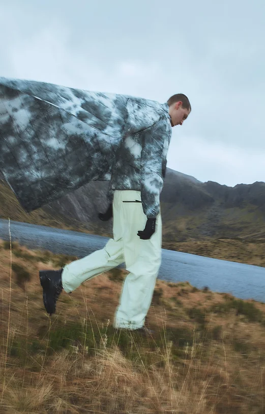 Man wearing a jacket with an "ice dye" pattern, walking through a wild landscape
