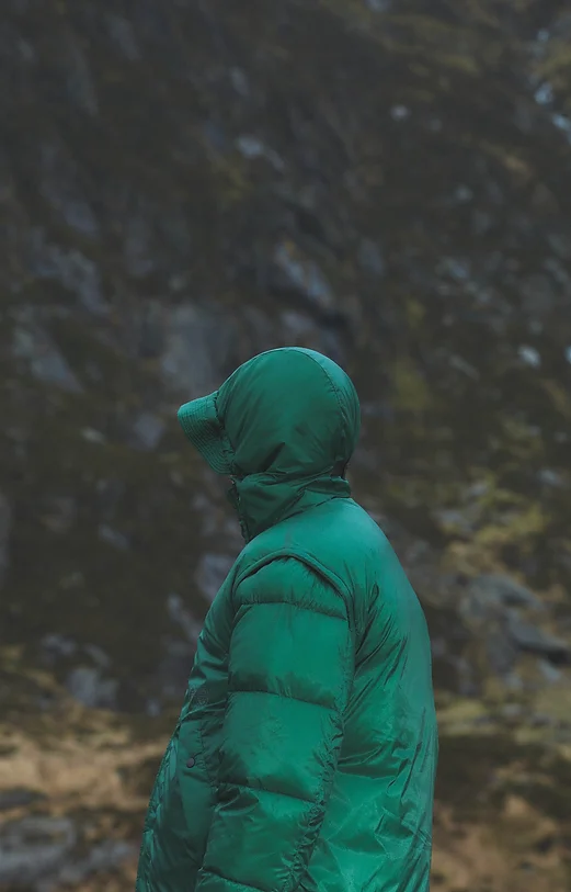 Man wearing a green puffer jacket standing in a mountainous landscape