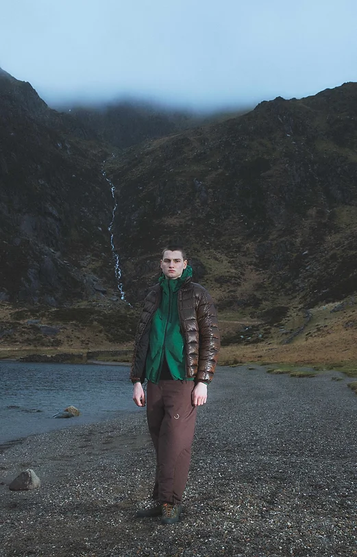 Man wearing a brown puffer jacket standing in a wilderness landscape