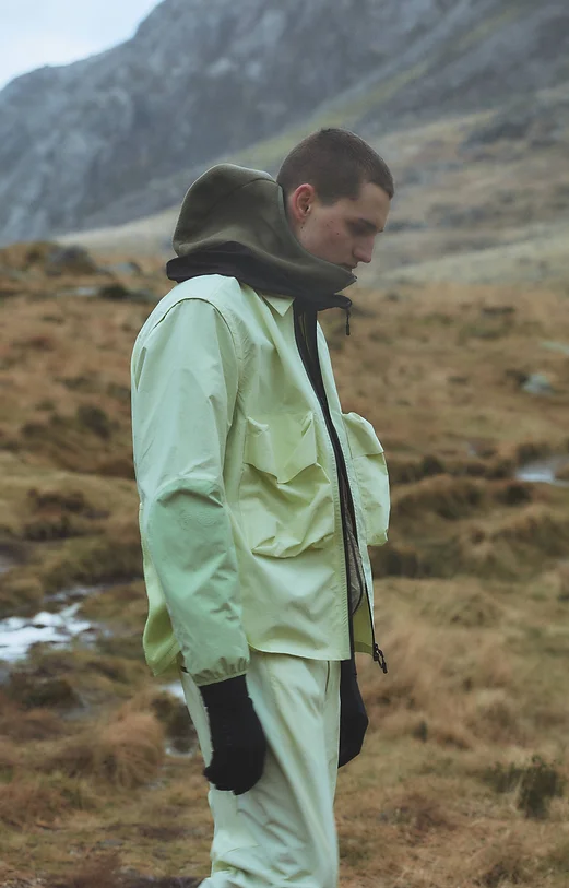 Man wearing a pale lime waterproof jacket walking through the mountains