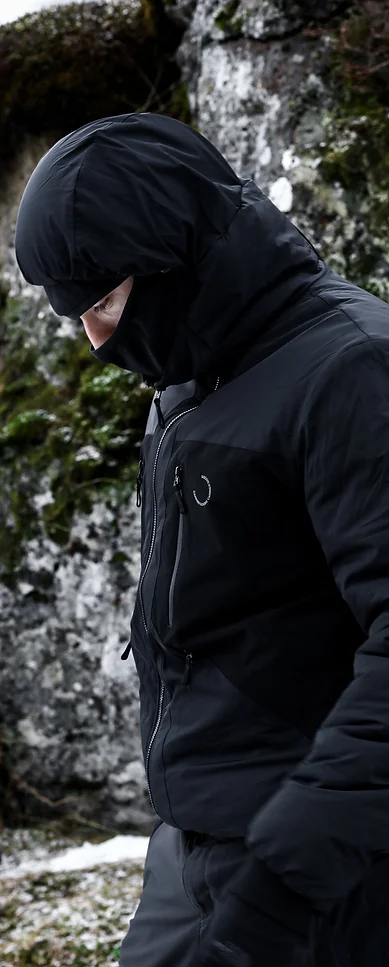 Man wearing a black jacket and hood, standing in a mountainous landscape