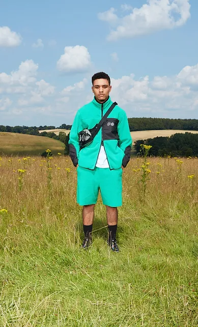 Man wearing bright green jacket and shorts, standing in a sunny field
