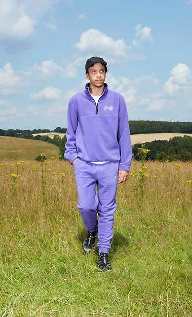 Man wearing a purple top and trousers, walking through a field