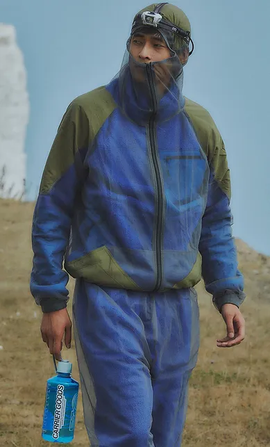 Man wearing zip-up top and trousers, carrying a water bottle and walking along chalk cliffs