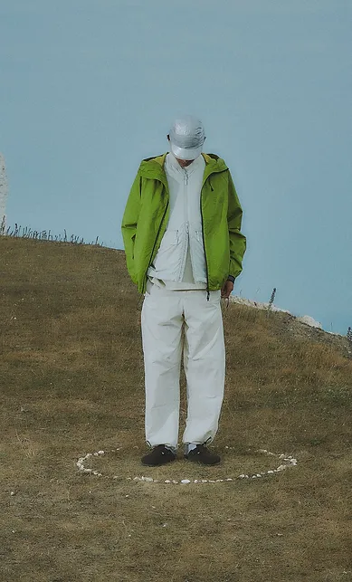 Man wearing a green jacket and white cap, standing on a hill