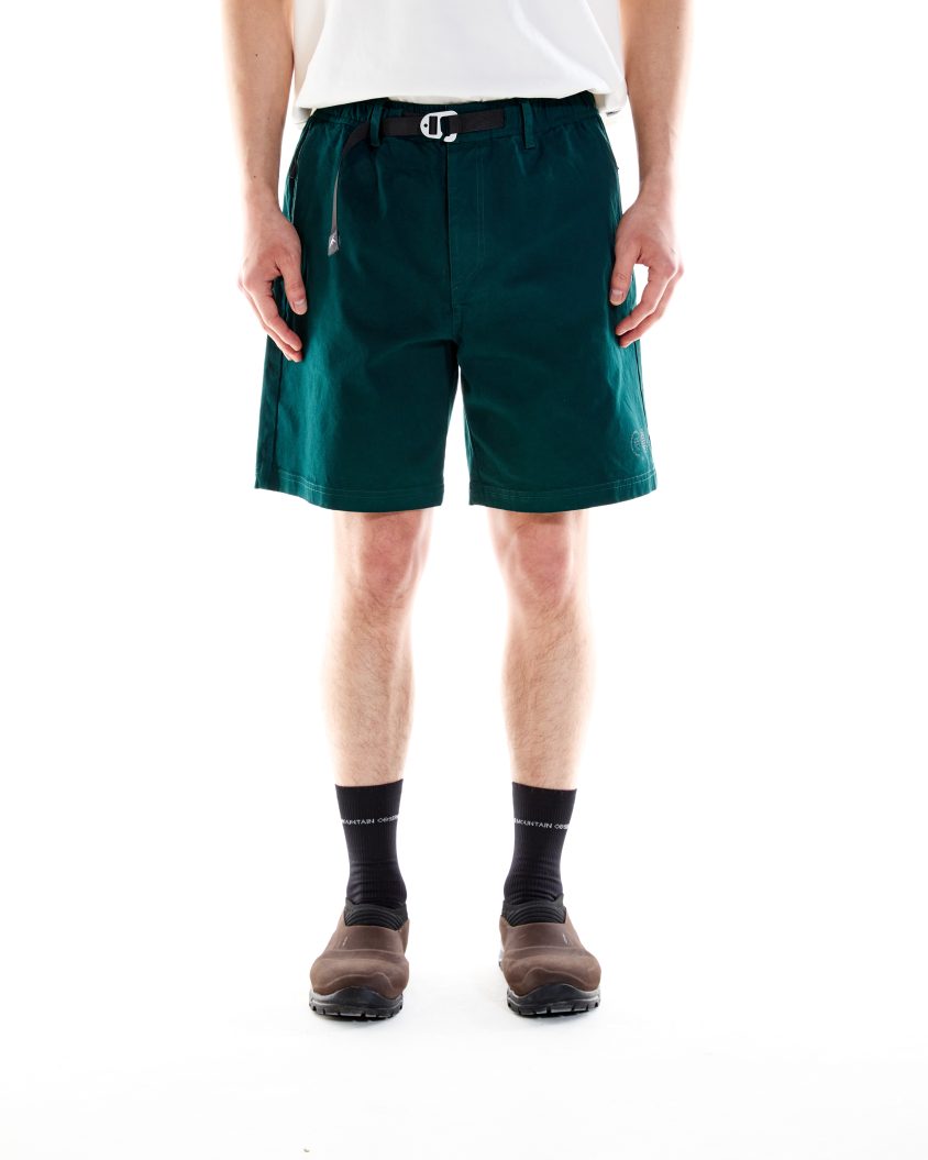 Model wearing Trek Shorts Pine Green with built-in belt and cotton construction. Outdoor shorts designed for comfort, movement, and trail readiness.