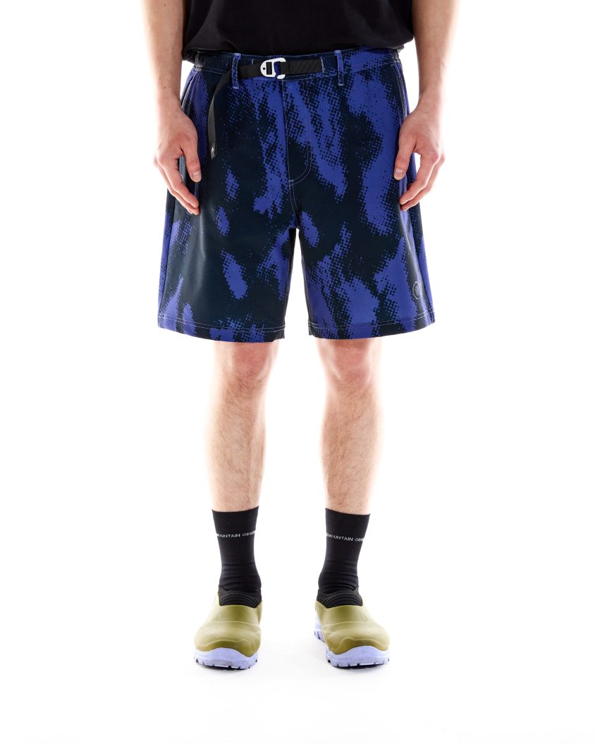 Model wearing PMO Trek Short in purple camo with built-in belt. Outdoor-ready shorts with front pockets and rear zip pocket.